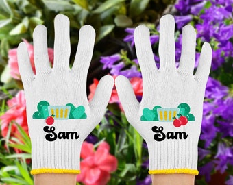 Op de afbeelding: Een paar witte tuinhandschoenen met een gele rand. De handschoenen hebben een groene en witte illustratie van een plant in een pot met rode appels en de naam "Sam" erop gedrukt.