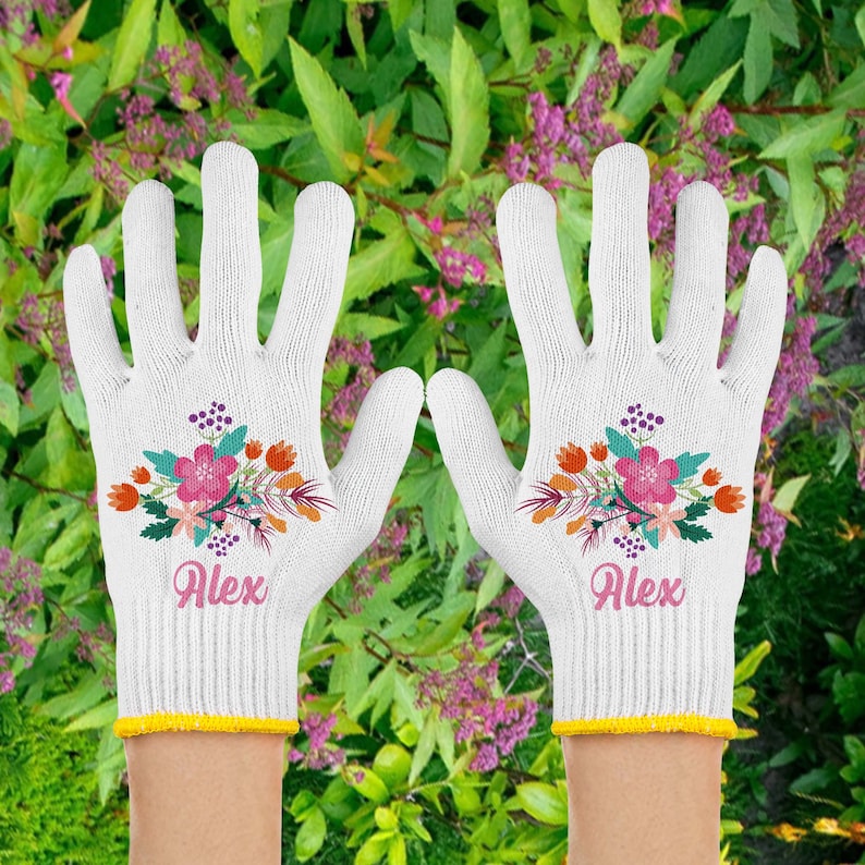 以下が含まれることがあります： 花柄のデザインと「Alex」という名前が刺繍された白いガーデニンググローブのペアです。