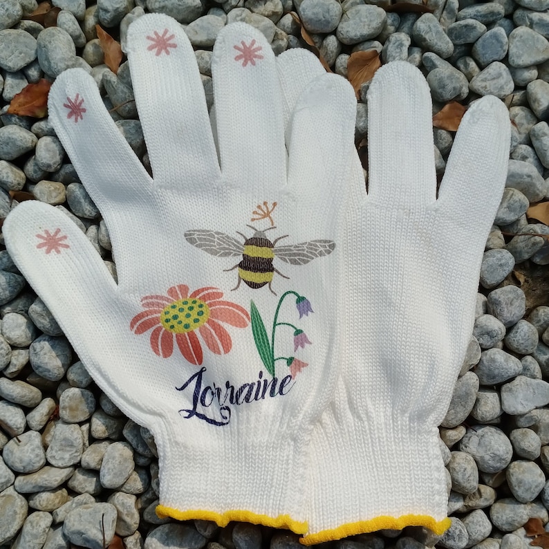 May include: White gardening gloves with a bee, flowers, and the name "Lorraine" printed on them.