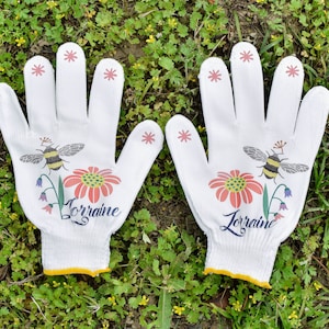 May include: A pair of white gardening gloves with yellow trim. The gloves have a bee and flower design with the name "Lorraine" printed on each glove.