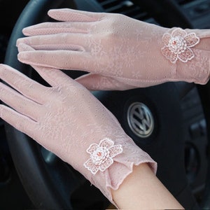 May include: A pair of delicate pink lace gloves with floral embellishments. The gloves are sheer and have a delicate floral pattern. The gloves are perfect for adding a touch of elegance to any outfit.