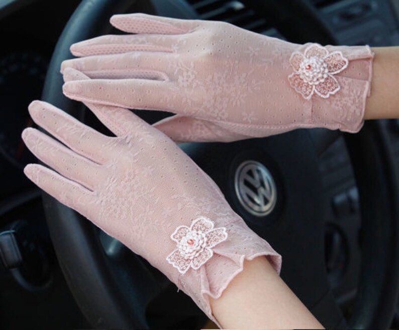 May include: A pair of delicate pink lace gloves with floral embellishments. The gloves are sheer and have a delicate floral pattern. The gloves are perfect for adding a touch of elegance to any outfit.