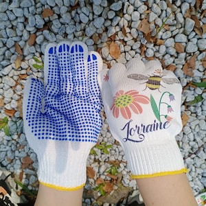 May include: Two pairs of white gardening gloves. One pair has blue dotted grip and the other has a floral design with a bee and the word "Lorraine".