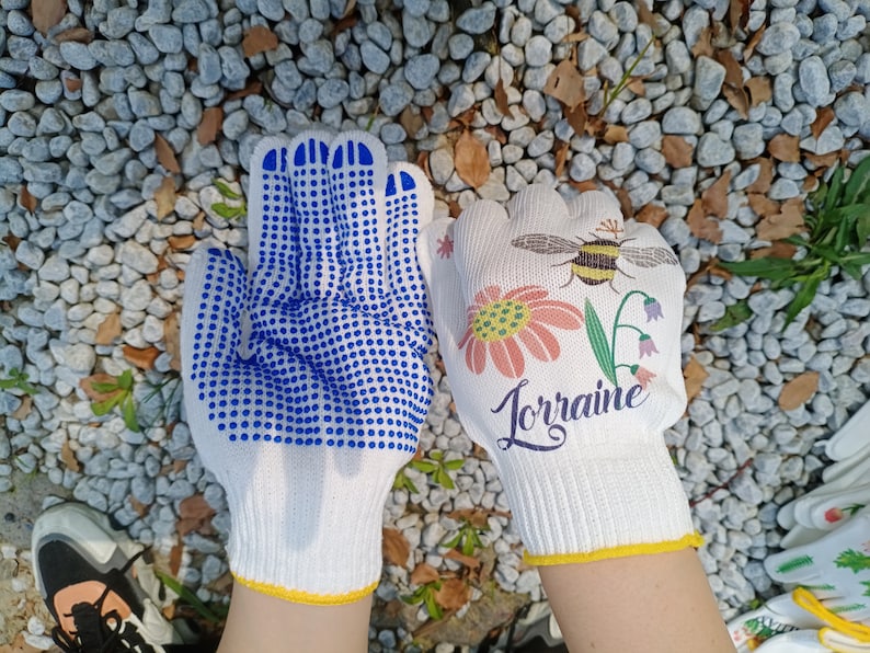May include: Two pairs of white gardening gloves. One pair has blue dotted grip and the other has a floral design with a bee and the word "Lorraine".