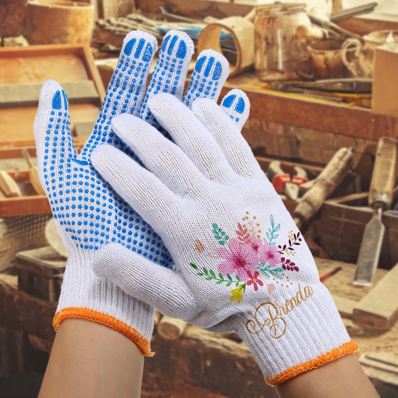 May include: White cotton work gloves with blue dotted grip on the palms and fingers. One glove has a floral design and the name "Brenda" written in gold script.