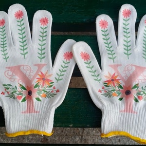 Könnte beinhalten: Ein Paar weiße Gartenhandschuhe mit einem rosafarbenen Blumendesign und dem Buchstaben "Y" auf jedem Handschuh.