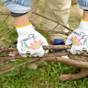 May include: A pair of white gardening gloves with a yellow trim. The gloves have a floral design with the word "remarkable" printed on them.