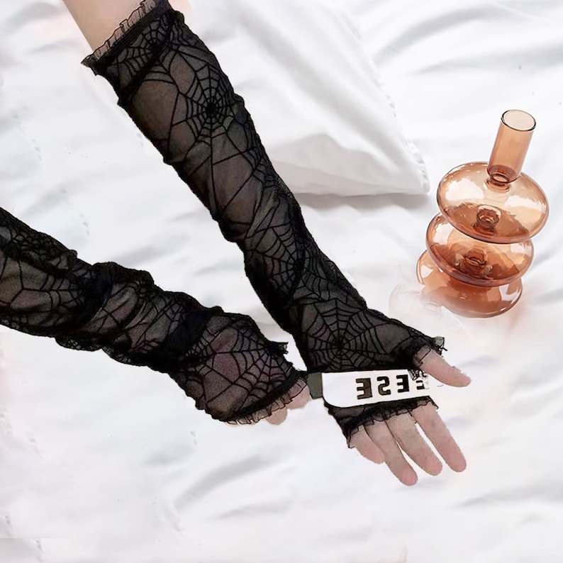 May include: A pair of black sheer fingerless gloves with a spiderweb pattern. The gloves have a ruffled edge and the word "EESE" is written on the back of one glove.