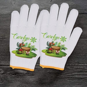 May include: A pair of white gardening gloves, each printed with the name "Carolyn" in green script. The gloves have a colourful illustration of a tree stump, mushrooms, and foliage. The cuffs are trimmed with yellow.