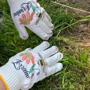 May include: A pair of white gardening gloves with a floral and bee design. The gloves are personalized with the name "Lorraine".