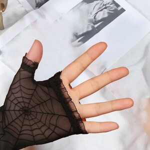 May include: Black fingerless gloves with a spiderweb design. The gloves have a ruffled edge.