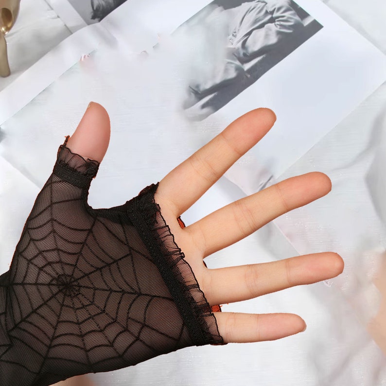 May include: Black fingerless gloves with a spiderweb design. The gloves have a ruffled edge.