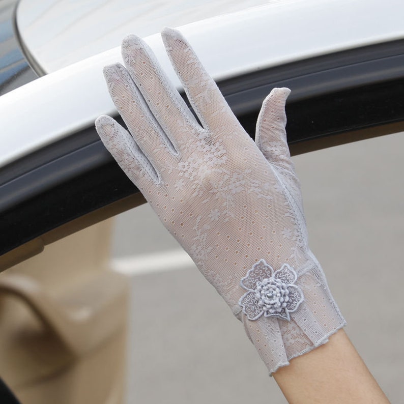 May include: A pair of gray lace gloves with a floral design on the wrist. The gloves are made of a sheer, delicate fabric.