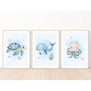 K&ouml;nnte beinhalten: Drei gerahmte Aquarell-Illustrationen von Meerestieren. Das erste Bild zeigt eine blaue Meeresschildkr&ouml;te, die im Meer schwimmt. Das zweite Bild zeigt einen blauen Wal mit wei&szlig;en Flecken, der im Meer schwimmt. Das dritte Bild zeigt einen hellvioletten Oktopus mit dunkelgrauen Tentakeln, der im Meer schwimmt.