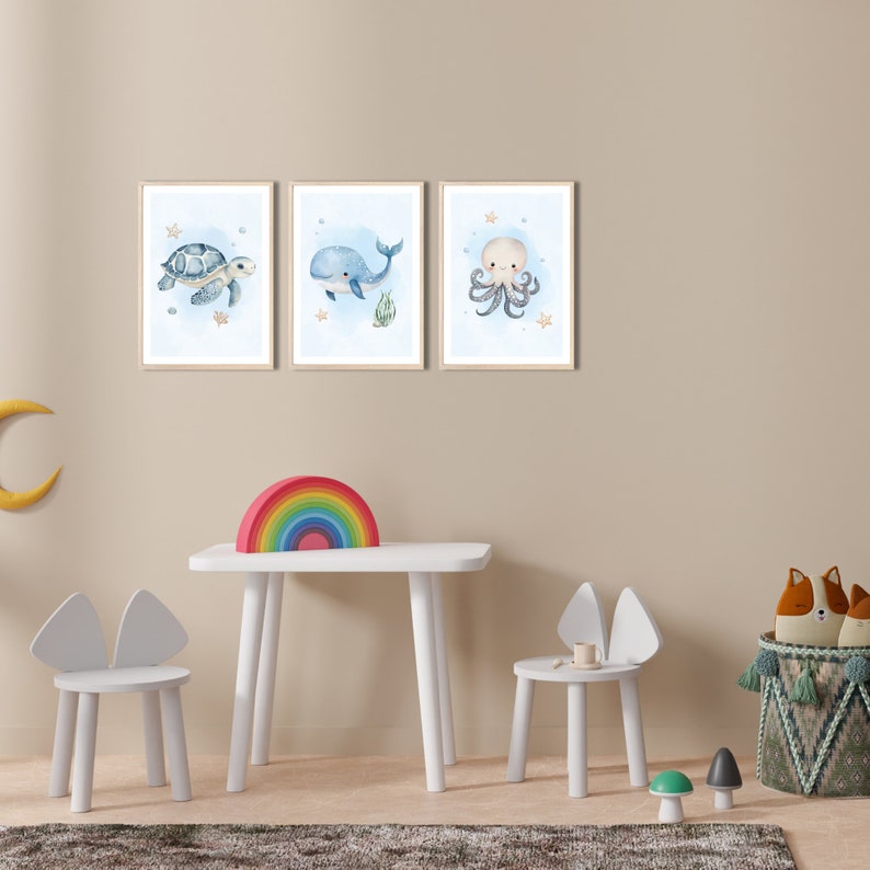 K&ouml;nnte beinhalten: Ein wei&szlig;er Tisch und zwei wei&szlig;e St&uuml;hle mit Hasenohren, ein Regenbogenbogen und drei gerahmte Aquarelldrucke von einer Schildkr&ouml;te, einem Wal und einem Oktopus an einer hellbeigen Wand.