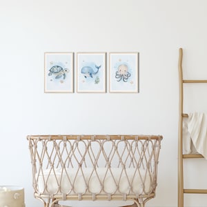 K&ouml;nnte beinhalten: Drei gerahmte Aquarell-Illustrationen von Meeresbewohnern an einer wei&szlig;en Wand. Die Illustrationen zeigen einen blauen Wal, eine Meeresschildkr&ouml;te und einen Oktopus. Die Illustrationen sind vor einem hellblauen Hintergrund mit wei&szlig;en Sternen und Muscheln platziert.