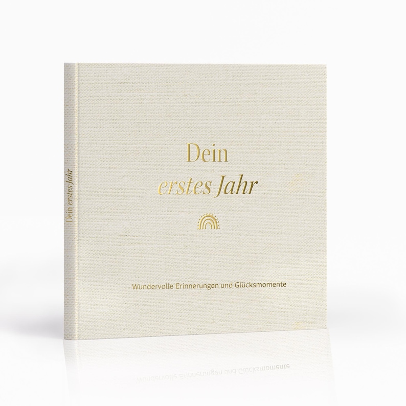 Op de afbeelding: Een beige boek met een linnenstructuur en gouden letters die "Dein erstes Jahr" (Je eerste jaar) lezen en een kleine gouden zon en regenboog afbeelding. De tekst "Wundervolle Erinnerungen und Gl&uuml;cksmomente" (Prachtige herinneringen en gelukkige momenten) staat onder de afbeelding.