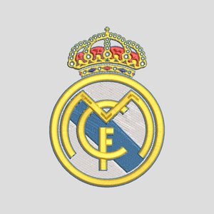 May include: Embroidered Real Madrid crest featuring a gold outline and a crown at the top. The crest includes the letters "MCF" in gold, with a blue diagonal stripe across the center. The design is set against a light gray background.