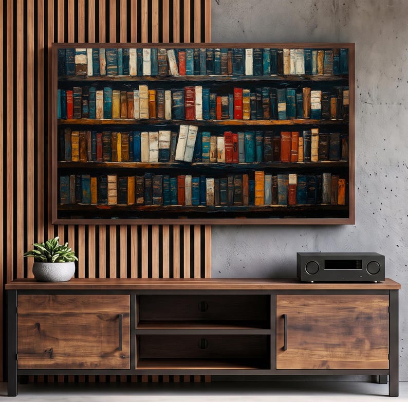 May include: A rectangular wall art print featuring a dense collection of multi-colored books arranged on dark wooden shelves. The artwork is displayed above a wooden media console with two cabinets and open shelving, next to a potted plant.