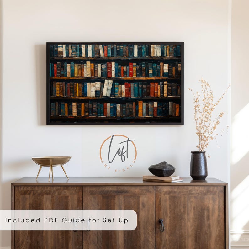 May include: A framed wall art print depicting a multi-shelf library filled with numerous colorful books in various shades of blue, red, yellow, and brown. The artwork is displayed above a wooden cabinet with a black vase and text.