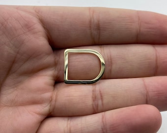 Puede incluir: Un anillo en D de metal dorado con un acabado liso.