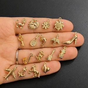 Puede incluir: Una colecci&oacute;n de peque&ntilde;os colgantes dorados de diversas formas: perro, cisne, llave, raqueta de tenis, delf&iacute;n, p&aacute;jaro, zapato de tac&oacute;n, saxof&oacute;n, guitarra, pi&ntilde;a, avi&oacute;n, ancla, caballo y coraz&oacute;n. Los colgantes se muestran sobre un fondo oscuro.
