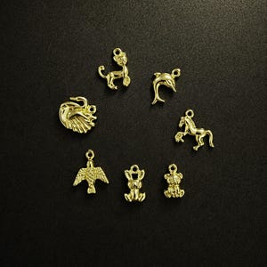 Puede incluir: Una colecci&oacute;n de peque&ntilde;os dijes dorados con formas de animales, incluyendo un le&oacute;n, un delf&iacute;n, un caballo, un &aacute;guila, un conejo y un oso. Los dijes est&aacute;n dispuestos sobre un fondo oscuro, mostrando sus intrincados detalles y acabado brillante.