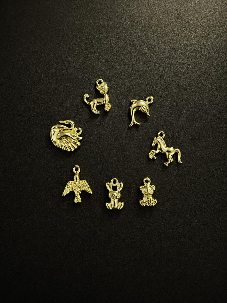 Puede incluir: Una colecci&oacute;n de peque&ntilde;os dijes dorados con formas de animales, incluyendo un le&oacute;n, un delf&iacute;n, un caballo, un &aacute;guila, un conejo y un oso. Los dijes est&aacute;n dispuestos sobre un fondo oscuro, mostrando sus intrincados detalles y acabado brillante.