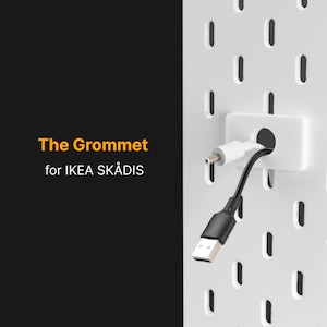 Könnte beinhalten: Weißer Kunststoff-Kabeldurchlass zur Organisation von Kabeln und Drähten auf einer weißen Lochwand. Der Durchlass hat ein Loch in der Mitte, durch das Kabel geführt werden können. Der Text "The Grommet for IKEA SKÅDIS" ist im Bild sichtbar.