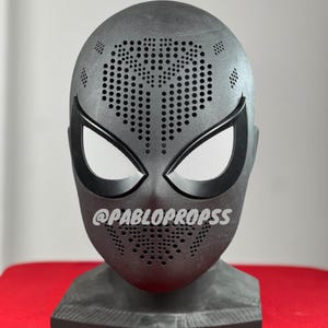 Op de afbeelding: Zwart en grijs Spider-Man masker met een zwart-wit patroon op het voorhoofd. Het masker staat op een zwarte standaard. De tekst "@PABLOPROPSS" staat op het masker.