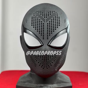 May include: A black Spider-Man mask with white mesh eye coverings and a perforated design on the forehead and mouth area. The mask is displayed on a stand. The text "@PABLOPROPS" is visible on the side of the mask.