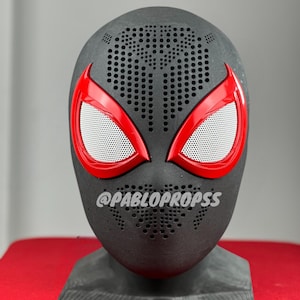 May include: Black and red Spider-Man mask with a textured surface and a white mesh over the eyes. The mask is on a black stand. The text "@PABLOPROPSS" is visible on the mask.