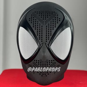 Op de afbeelding: Zwart Spider-Man-masker met een wit gaasooggebied en een zwart-wit spinnenontwerp. Het masker heeft een gestructureerd oppervlak met kleine gaatjes.