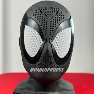 Op de afbeelding: Zwart Spider-Man-masker met een wit gaasoogstuk en een zwarte standaard. Het masker heeft een gestructureerd oppervlak met kleine gaatjes. De tekst "@PABLOPROPSS" is op het masker gedrukt.