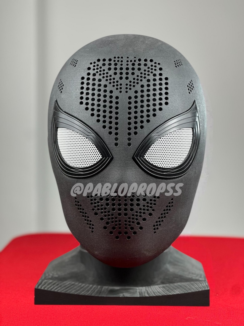 May include: Black Spider-Man mask with a textured surface and a pattern of small holes. The mask has a black and white spider design on the front and the text "@PABLOPROPSSS" on the chin.