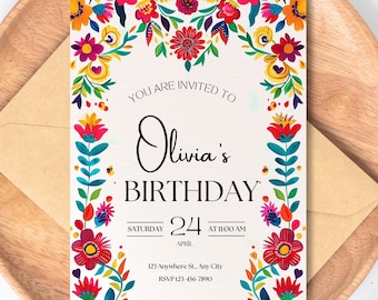 Puede incluir: Una colorida invitación de cumpleaños con borde floral. La invitación dice "Estás invitado/a al cumpleaños de Olivia" con la fecha, hora y detalles de la ubicación. La invitación está sobre un plato de madera con un sobre marrón.