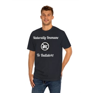 May include: A dark blue t-shirt with white text that reads "Naturally Immune" and a white graphic of a bull with a red circle and line through it. The text below the graphic reads "To Bullsh#t".