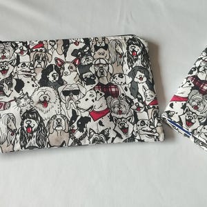 Può includere: Un set di due accessori a tema cani: una pochette con cerniera e cinturino da polso e un piccolo portafoglio pieghevole. Entrambi gli articoli presentano un motivo ripetuto di varie razze di cani in bianco, nero e grigio, con accenti rossi.