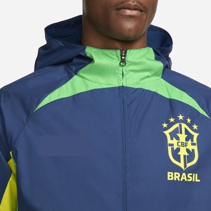 以下が含まれることがあります： ジッパー留めのネイビーとグリーンのウィンドブレーカー。ブラジル代表チームの紋章と「CBF」と「BRASIL」の文字がデザインされています。