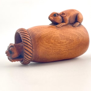Puede incluir: Una escultura de madera tallada de un ratón y una rata. La rata está encima de un barril de madera, y el ratón está dentro del barril. La escultura está hecha de madera de color marrón claro y tiene tallas detalladas.