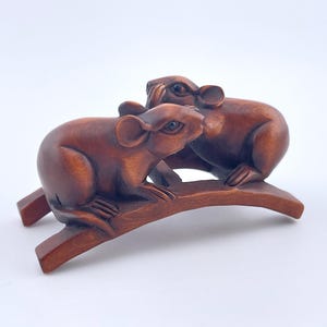 May include: A wooden sculpture of two brown rats perched on a curved branch. The rats are carved with detailed features, including ears, eyes, and whiskers. The sculpture is set against a white background.