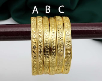 May include: Six gold bangles with intricate floral and leaf patterns. The bangles are displayed on a dark brown rod against a white background, with a dark green fabric in the background. The letters "A", "B", and "C" are visible.