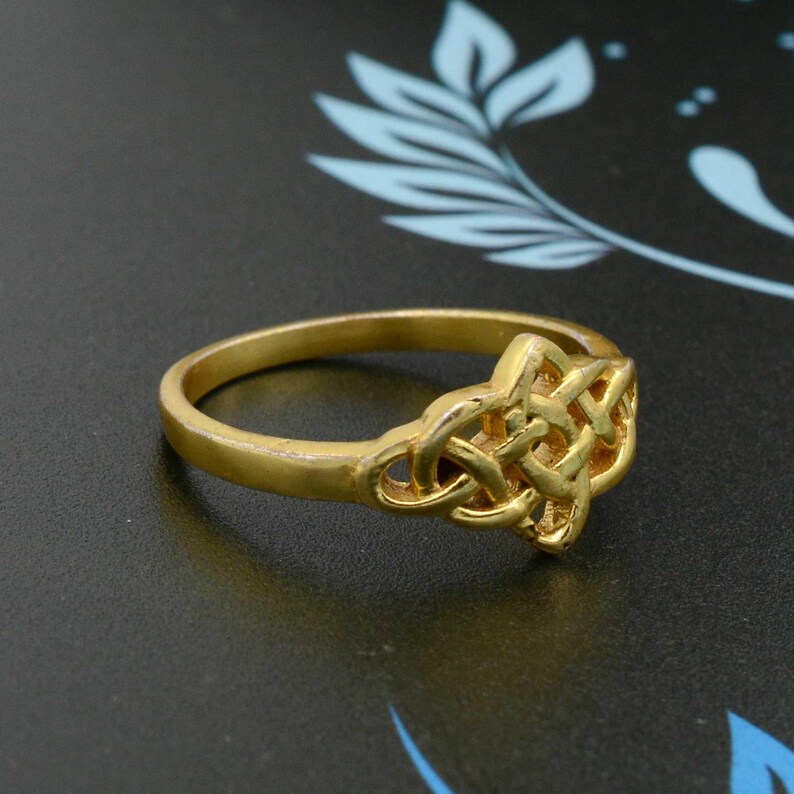 May include: A gold-coloured ring featuring a Celtic knot design. The ring is simple and elegant.