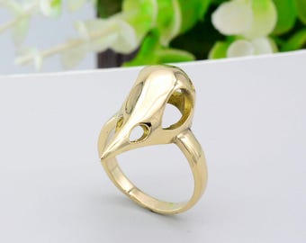 May include: A gold-colored ring with a bird skull design. The skull is hollow and has eye sockets.