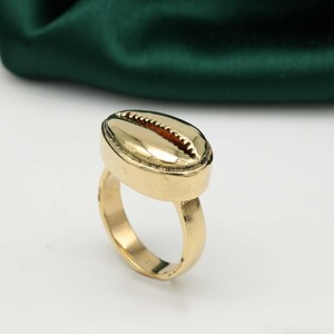 Könnte beinhalten: Ein goldfarbener Ring mit Muschel-Design. Der Ring ist aus Metall und hat eine glatte Oberfläche.