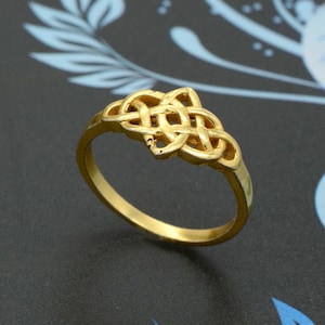 May include: A gold ring featuring a Celtic knot design. The ring is simple and elegant.