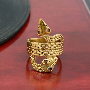 Könnte beinhalten: Ein goldfarbener Ring mit einem detaillierten Schlangendesign. Die Schlange ist um den Ringband gewickelt, wobei Kopf und Schwanz die Oberseite des Rings bilden. Die Schuppen der Schlange sind aufwendig gestaltet und verleihen dem Ring ein strukturiertes Aussehen.