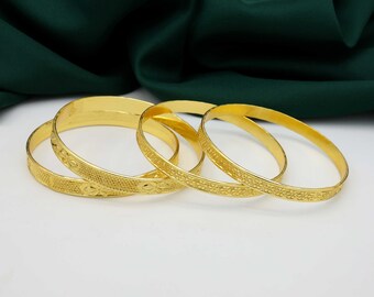 Könnte beinhalten: Vier goldfarbene Armreifen mit aufwendigen Blumenmustern. Die Armreifen sind übereinander gestapelt.