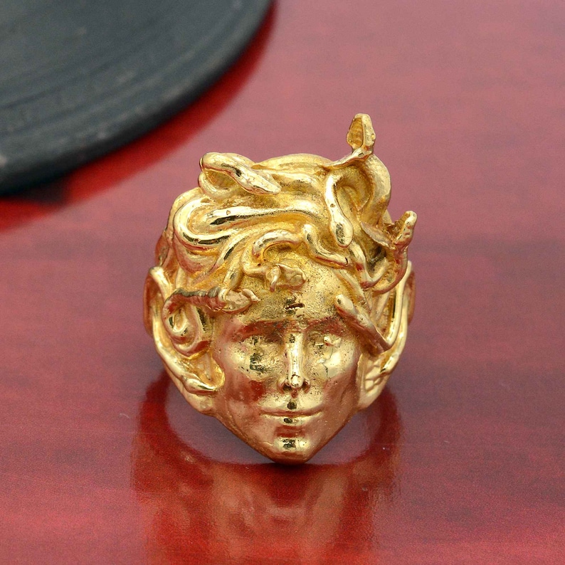 May include: A gold-colored ring featuring a detailed sculpture of Medusa's head with snakes for hair.