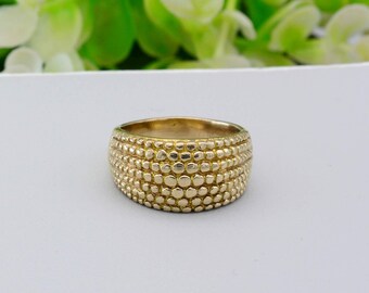 May include: A gold-colored ring with a wide band. The ring's surface is textured with a pattern of small, raised circles. The ring is a statement piece, suitable for everyday wear or special occasions.